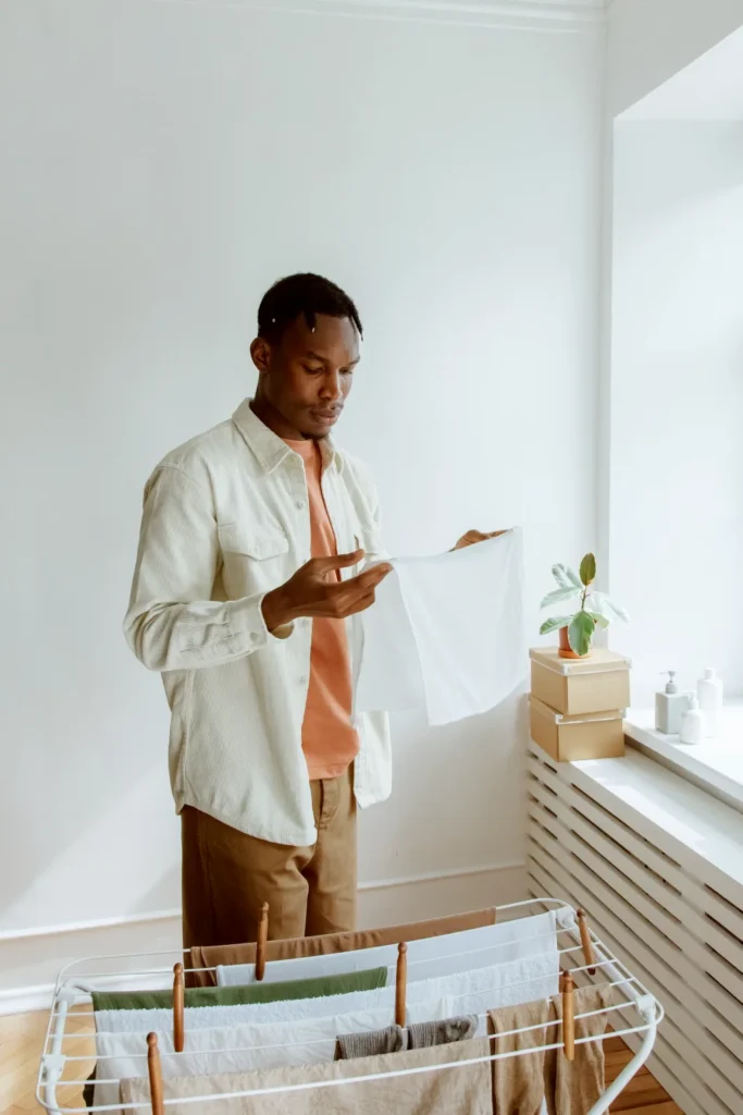 Man hanging fresh laundry on a rack in a bright room
