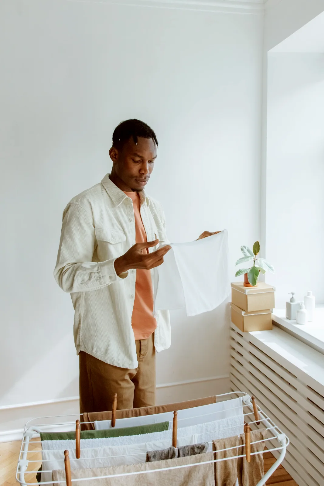 Man hanging fresh laundry on a rack in a bright room